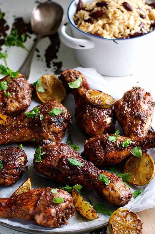 Jerk chicken thighs with dark charred spiced crust and grill marks on a platter with lime and Scotch bonnet