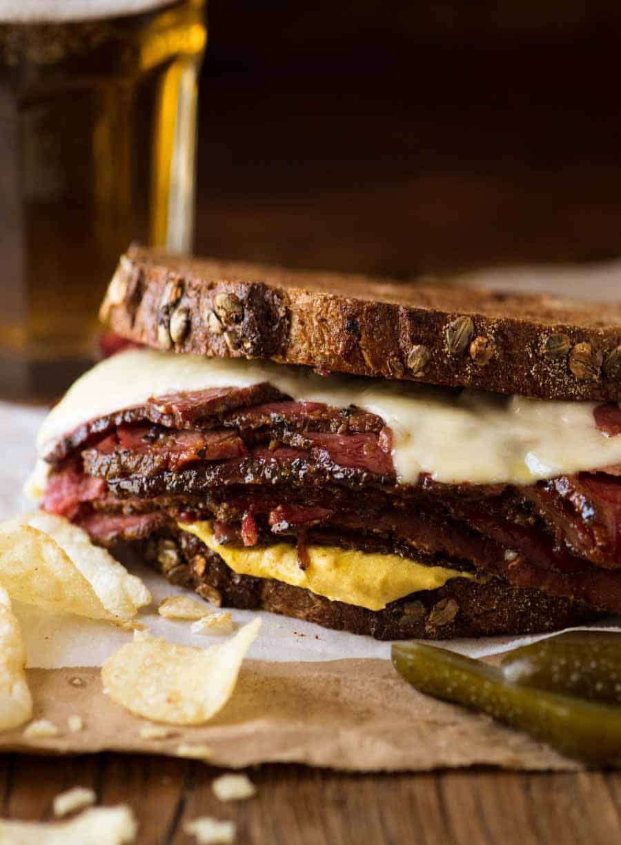 Easy Homemade Pastrami on rye bread with crisps and pickles on the side with a beer in the background