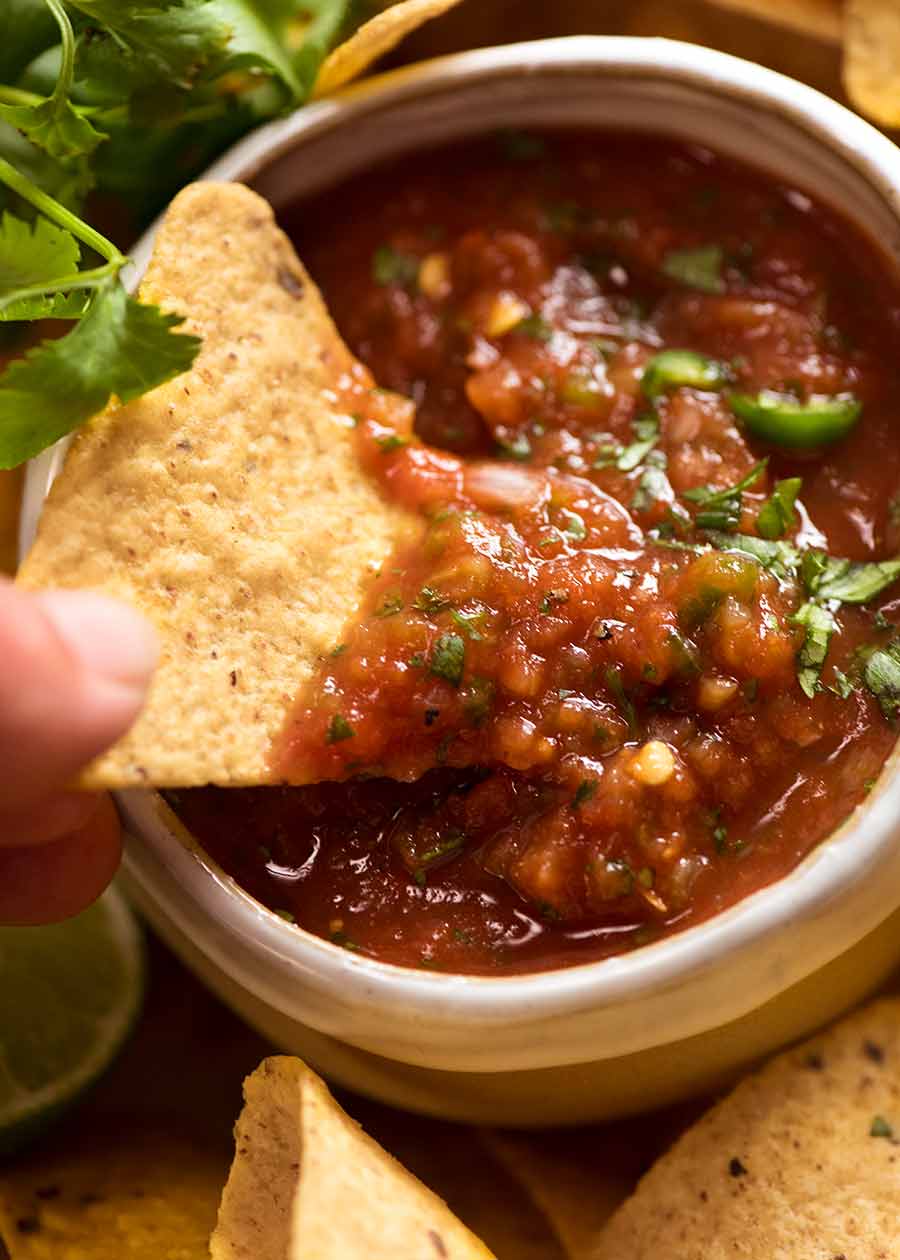 Close up of corn chip scooping up homemade salsa (Salsa recipe - restaurant style)