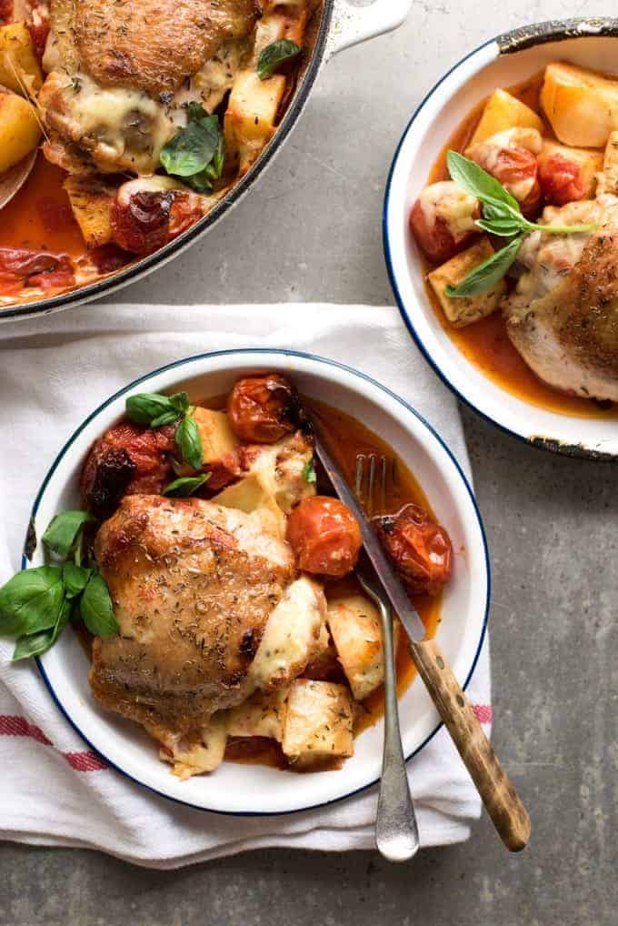 Baked Italian Chicken with Potatoes and cherry tomatoes in a bowl with a knife and fork, ready to be eaten.