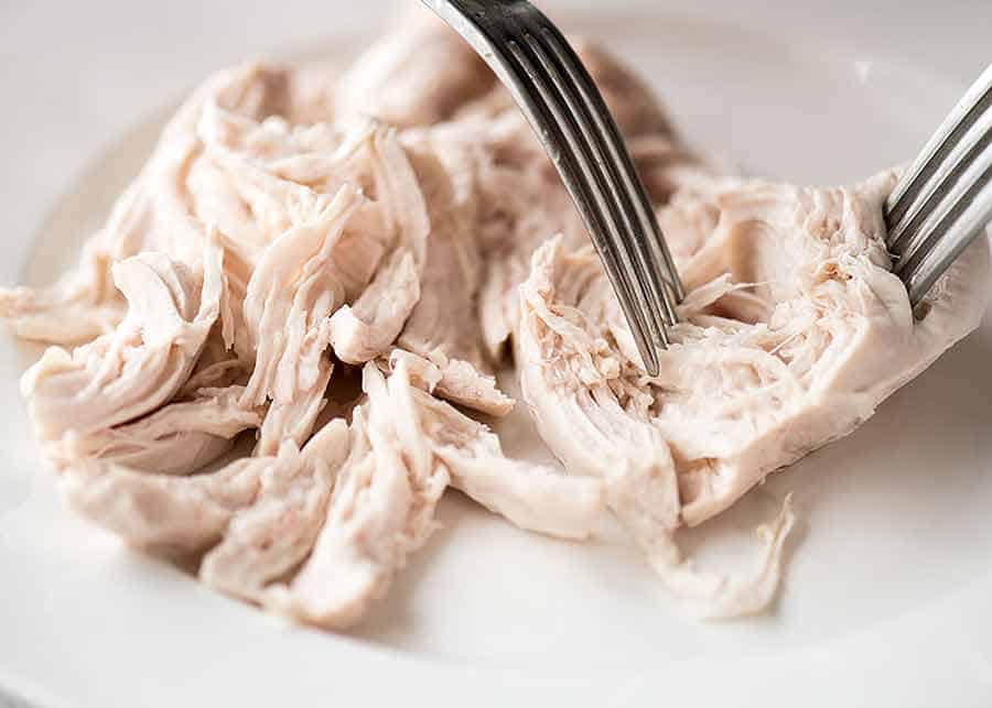 Two forks shredding cooked chicken