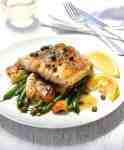 Fish Piccata with smashed potatoes and steamed greens on a white plate with lemon wedges, ready to be eaten.