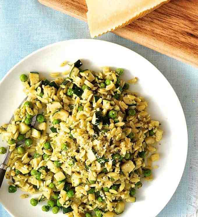 Pea, Zucchini and Pesto Orzo / Risoni on a white plate with parmesan on the side.