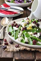 Dressing being poured over a Christmas Salad made with snow peas, asparagus, beans, feta and cranberries. Colours of Christmas!