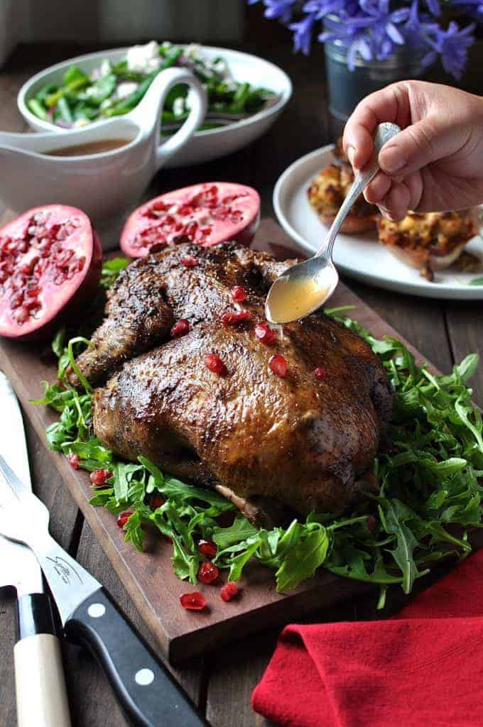Festive Christmas Roast Duck sitting on a bed of rocket salad garnished with pomegranate seeds on a wooden board, ready for carving.