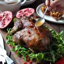 Festive Christmas Roast Duck sitting on a bed of rocket salad garnished with pomegranate seeds on a wooden board, ready for carving.