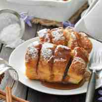 Hasselback Baked French Toast on a white plate, dusted with icing sugar and drizzled with maple syrup.