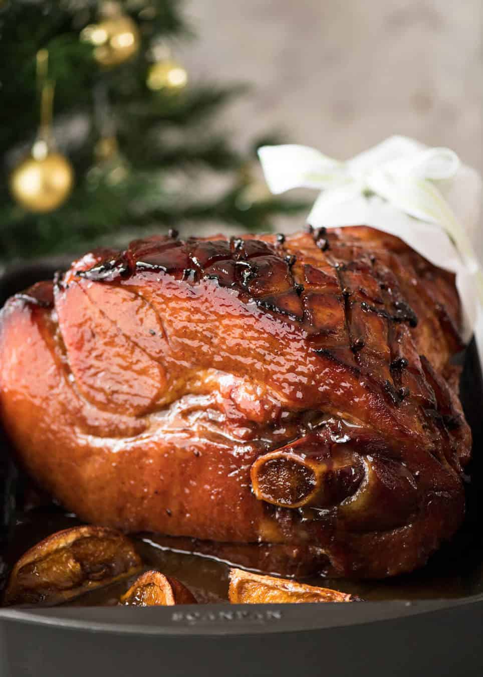 A baked ham shining with a brown maple sugar icing in a large white dish.