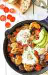 Chorizo Breakfast Hash with crispy smashed potatoes and eggs in a cast iron skillet with avocado on the side.