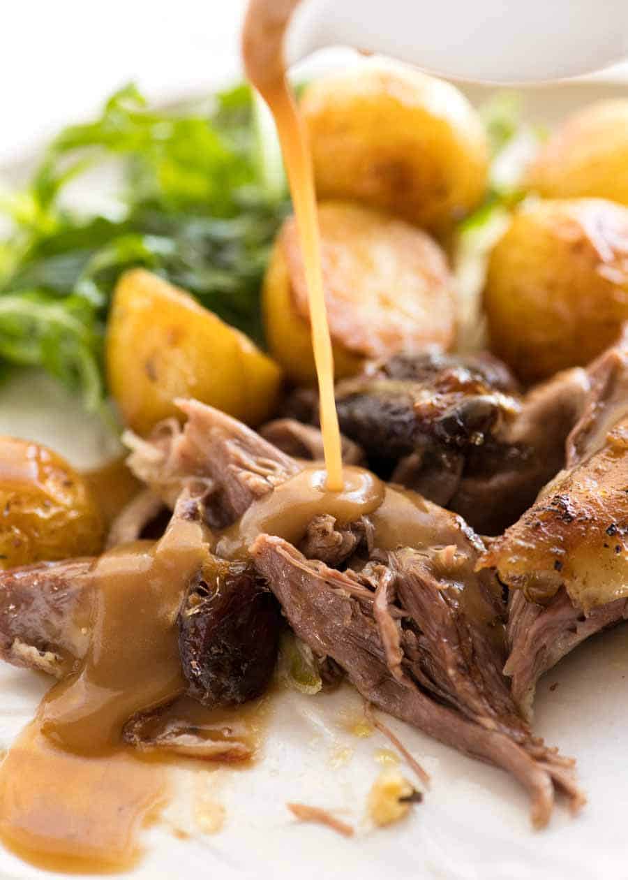 Sauce that is poured over the shoulder of lamb cooked over low heat on a plate with a side of roasted potatoes and salad, ready to eat