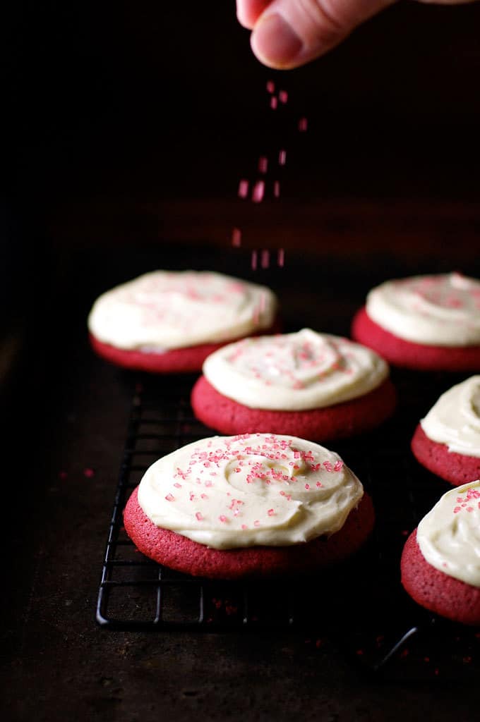 Sprinkling finishing touches on Red Velvet Cookies with Cream Cheese Frosting