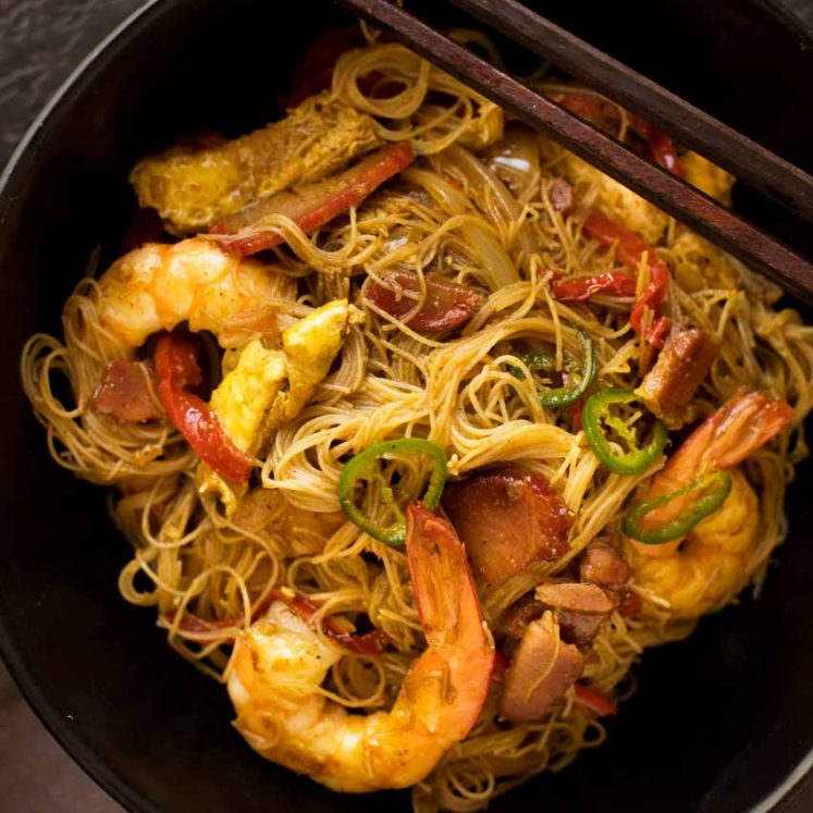 Overhead photo of Singapore Noodles in a black bowl with chopsticks resting on the edge, ready to be eaten.