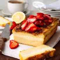 Cream Cheese Stuffed French Toast Loaf topped with strawberries, sliced on a board