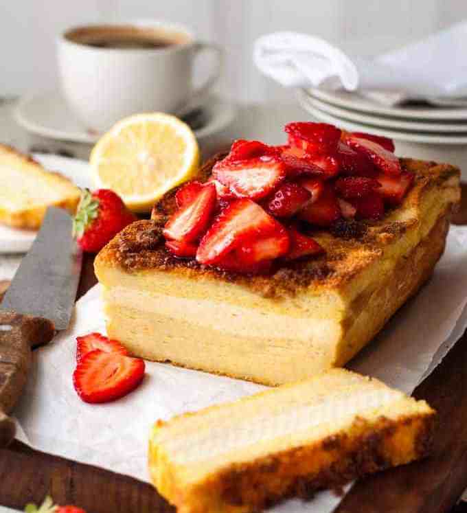 Cream Cheese Stuffed French Toast Loaf topped with strawberries, sliced on a board