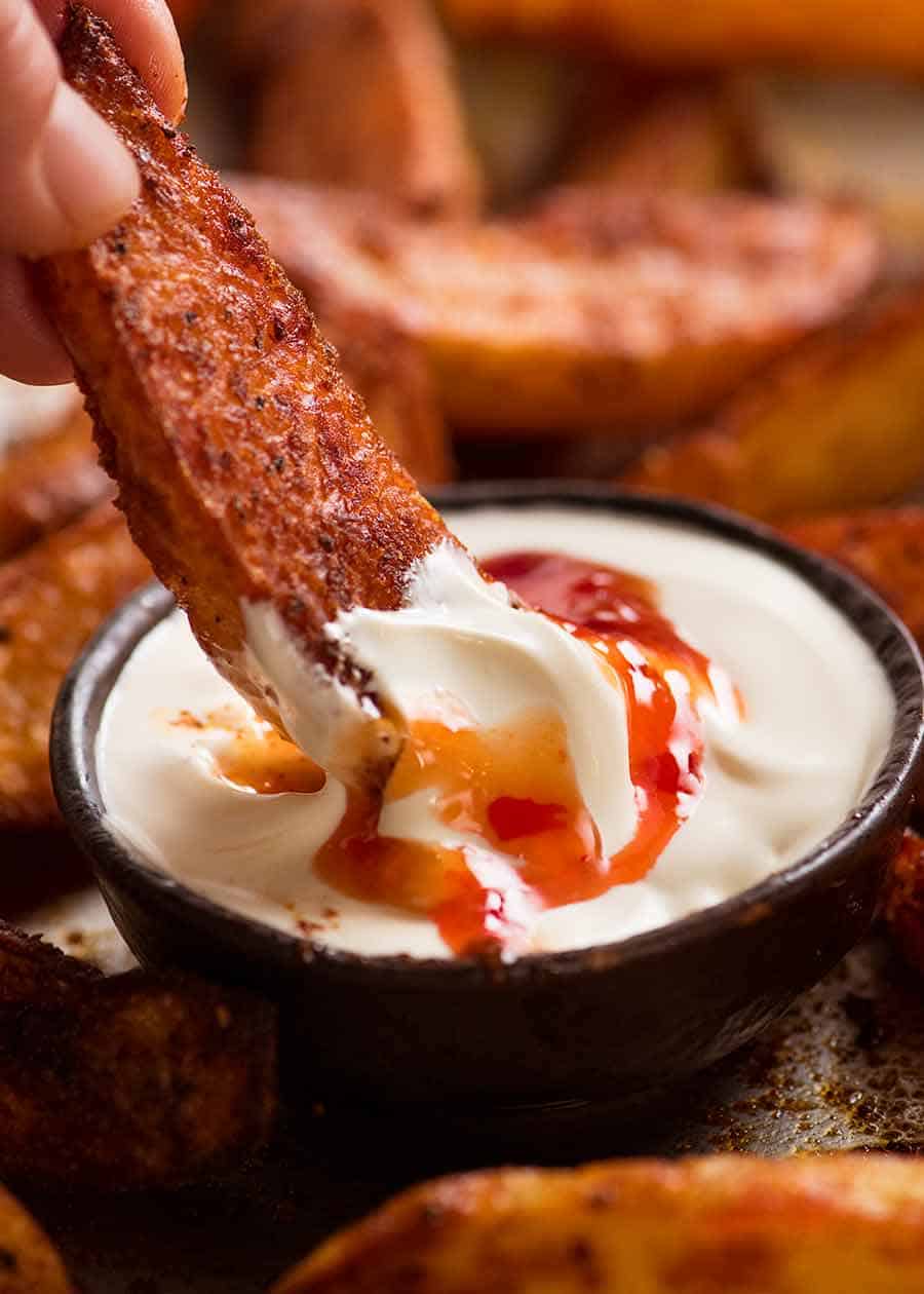 Dipping crunchy baked potato wedges into sour cream and sweet chilli sauce