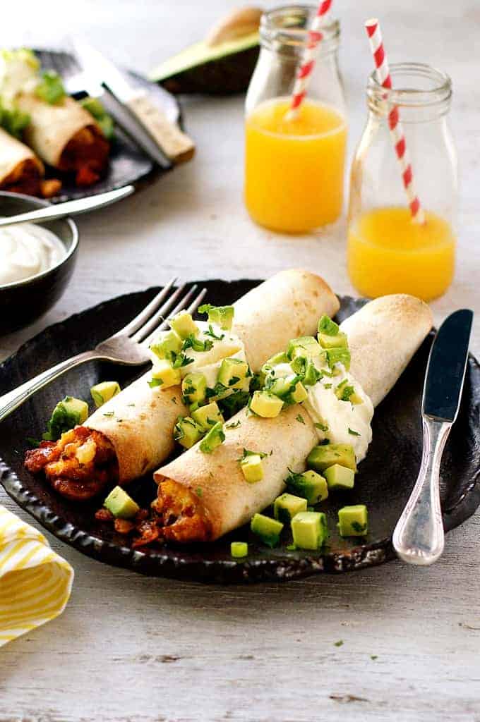 Bacon and Egg Breakfast Enchiladas topped with avocado, with orange juice in background