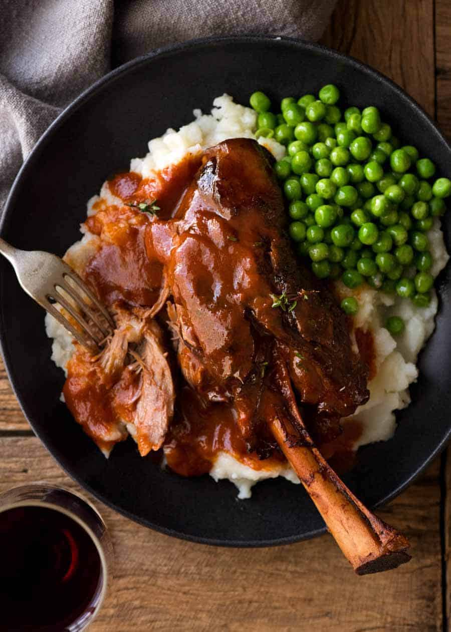 Overhead photo of Slow Cooked Lamb Shanks in Red Wine Sauce served over creamy mashed potato with a side of peas, ready to be eaten