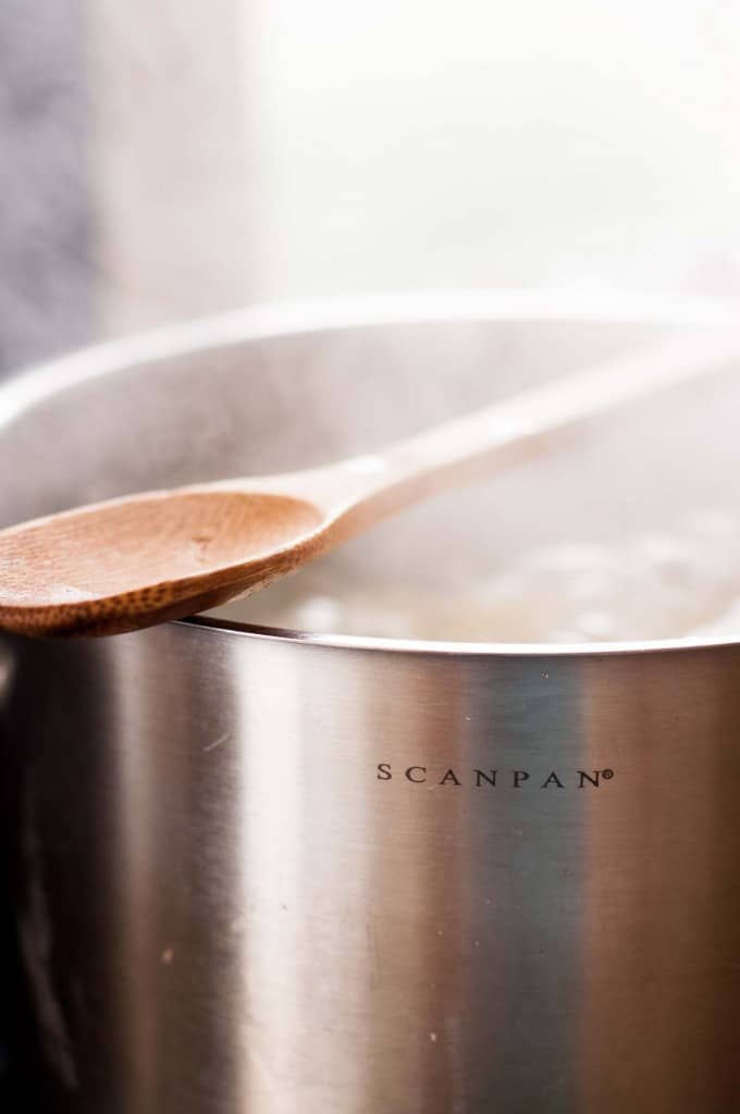 Wooden spoon resting on a bubbling pot to stop it from boiling over.