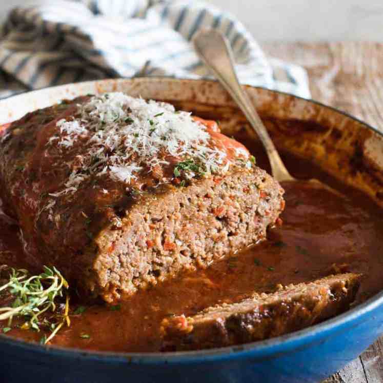 Italian Meatloaf with tomato marinara sauce in a round blue casserole pan with the end sliced off, revealing the juicy inside.