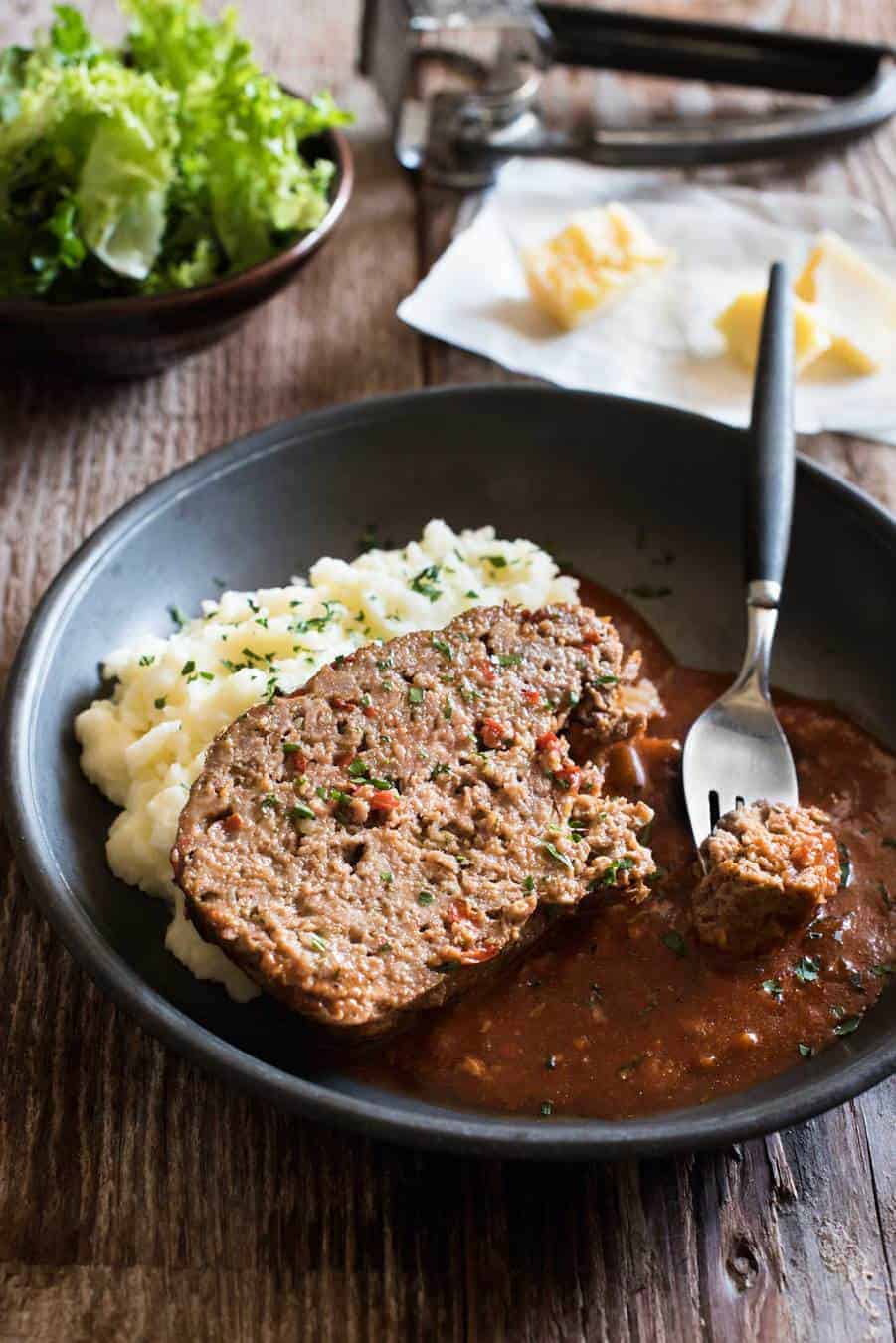 A slice of Italian meatloaf on creamy mashed potato, drizzled with tomato marinara sauce the meatloaf was cooked with.