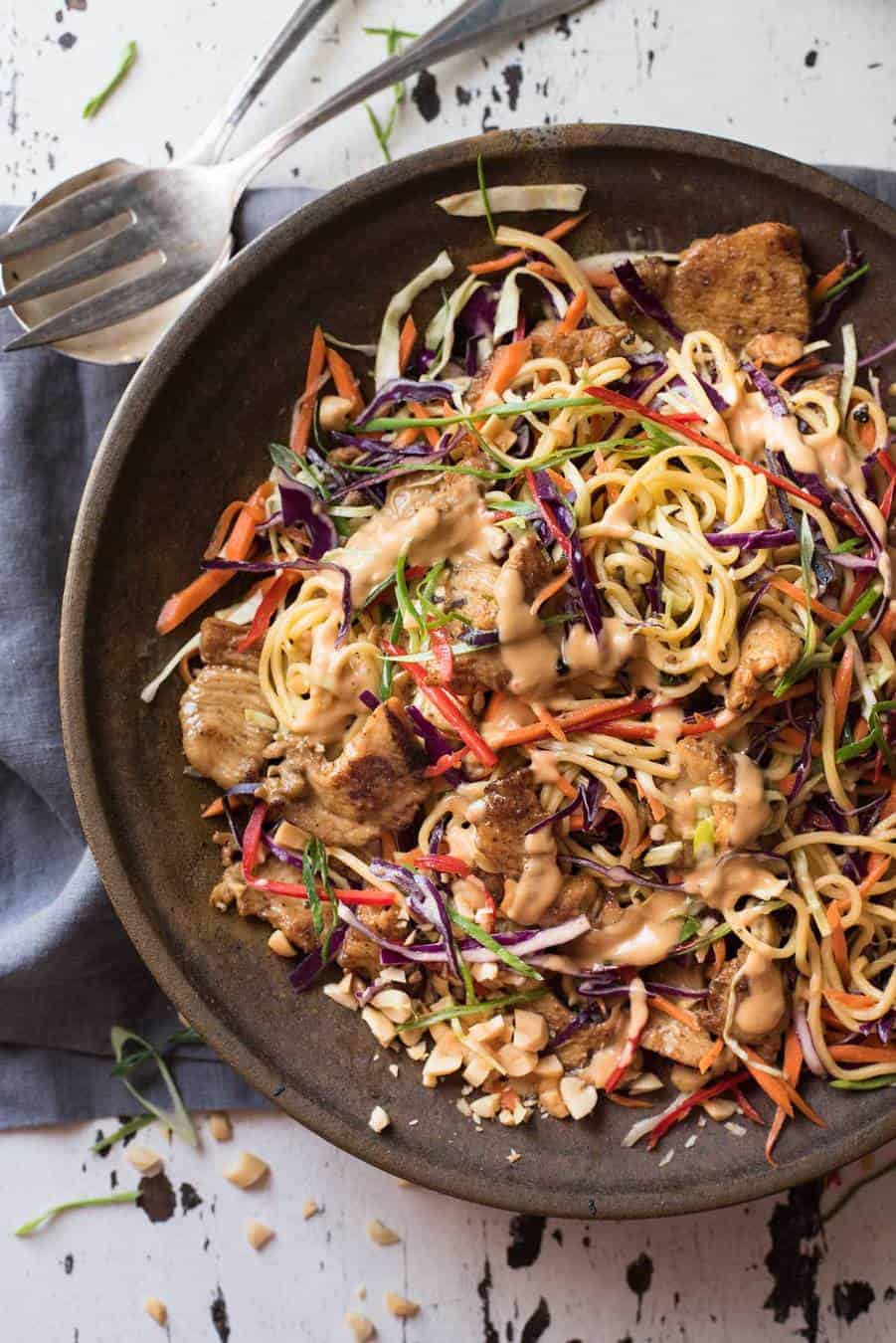 Satay Chicken Noodle Salad drizzled with peanut dressing in a dark brown bowl, ready to be served.
