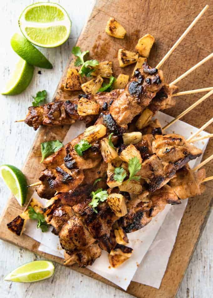 A stack of Pineapple Coconut Hawaiian Chicken Skewers on a wooden board with lime wedges.