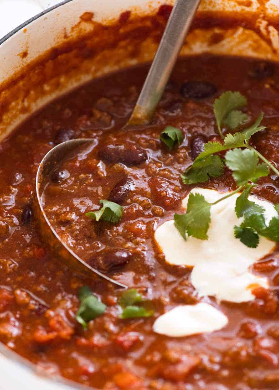 Close up of Chili Con Carne in a white pot being scooped up with a ladle, ready to be served