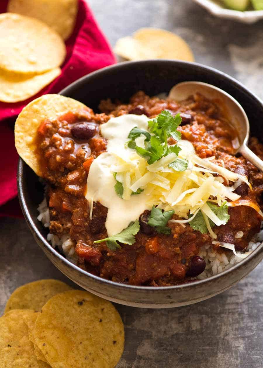 Chili Con Carne served over rice with sour cream, grated cheese and cilantro garnishes, ready to eat