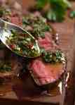Close up of spoon drizzling Chimuchurri Sauce on steak