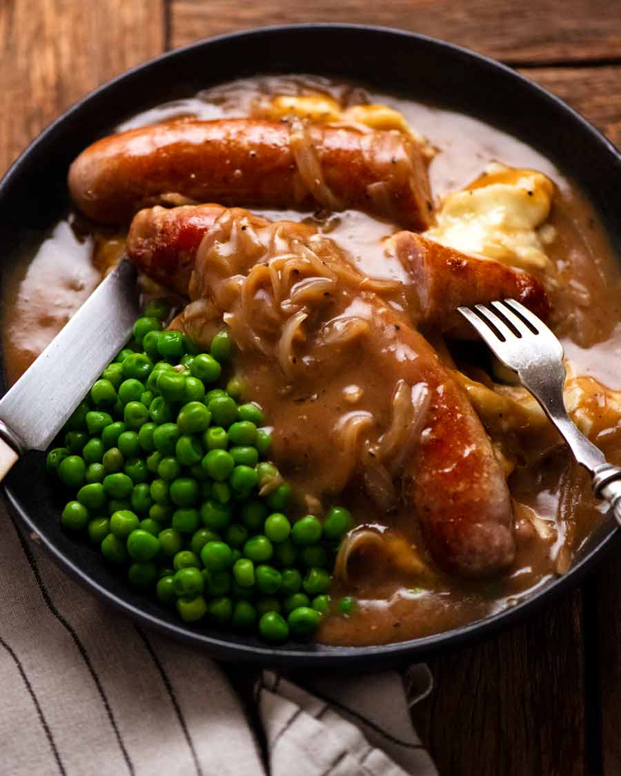 Bangers and Mash (Sausage with Onion Gravy) on a plate with mashed potato and peas
