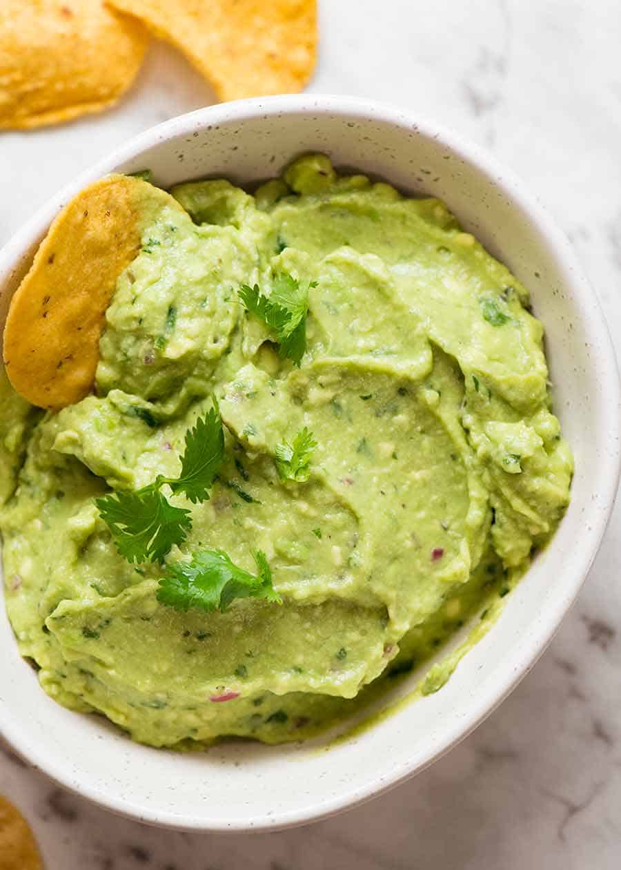 Guacamole in a white bowl with corn chips, ready to be eaten