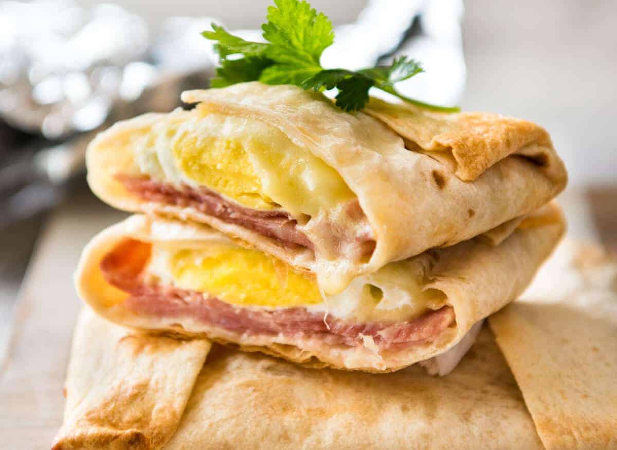 Stack of hot Ham, Egg and Cheese Pockets made with tortillas cut to show the inside with molten cheese and perfectly cooked egg.