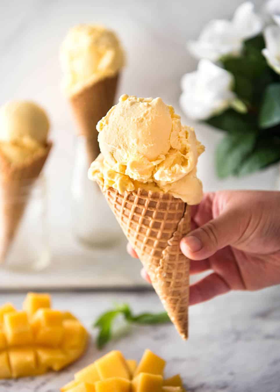 Ice cream cone with mango ice cream held in a hand.