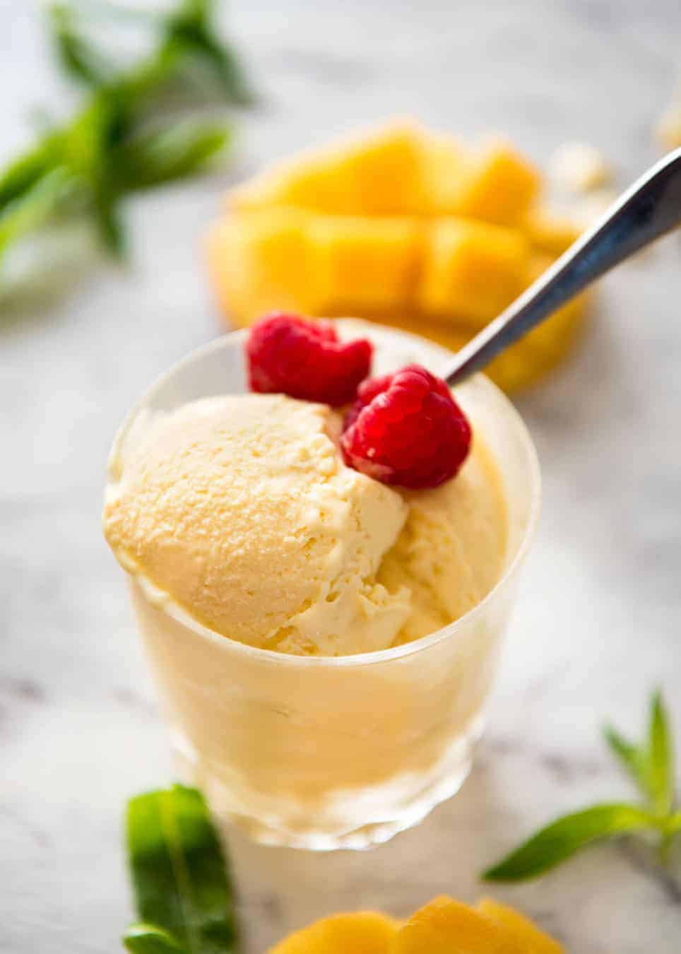 A glass with scoops of homemade Mango Ice Cream garnished with fresh raspberries.