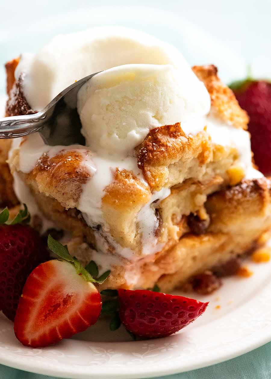 Close up of spoon cutting into a piece of Bread and Butter Pudding topped with ice cream