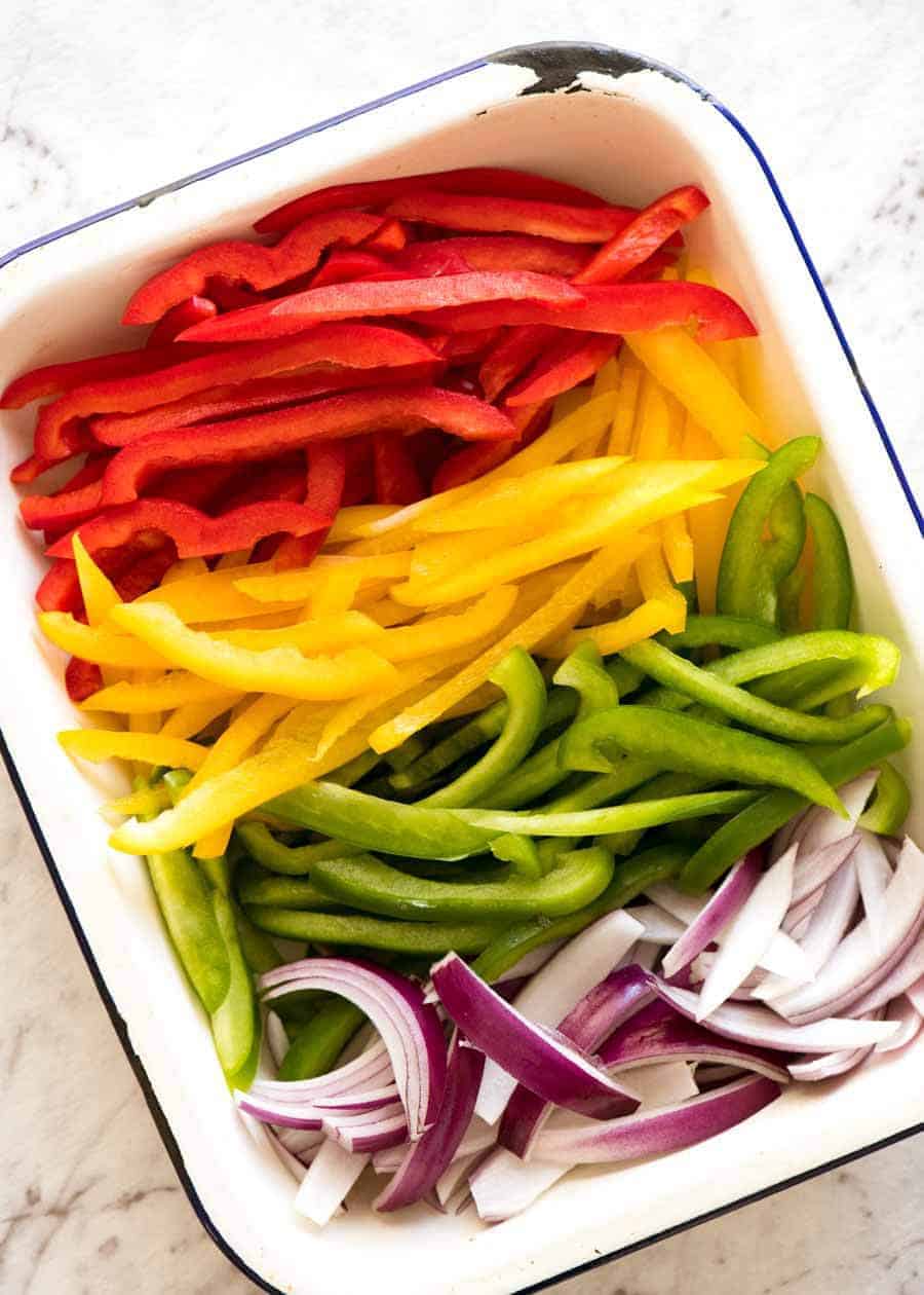 Sliced yellow, green and red peppers for Chicken Fajitas in a white enamel pan
