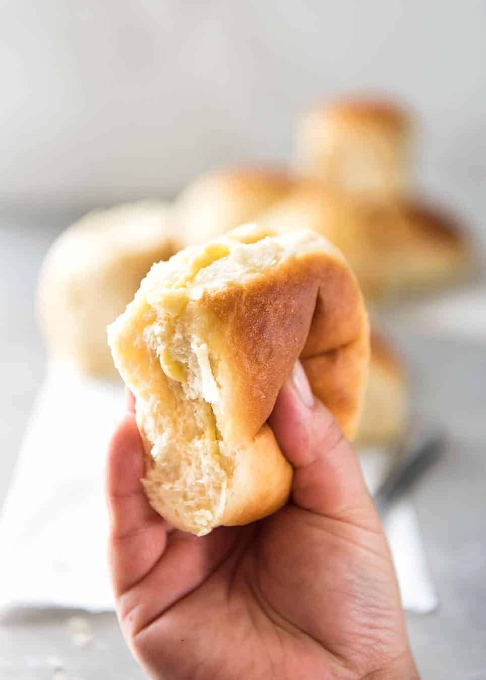 Hand squeezing no knead dinner rolls to show how soft and fluffy they are.