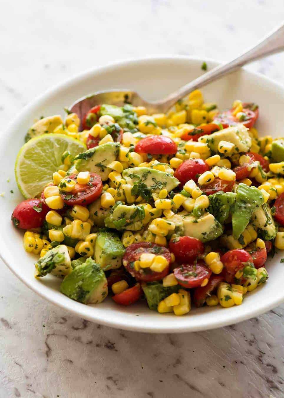 Corn Salad with Avocado in a white bowl with a spoon, ready to be served