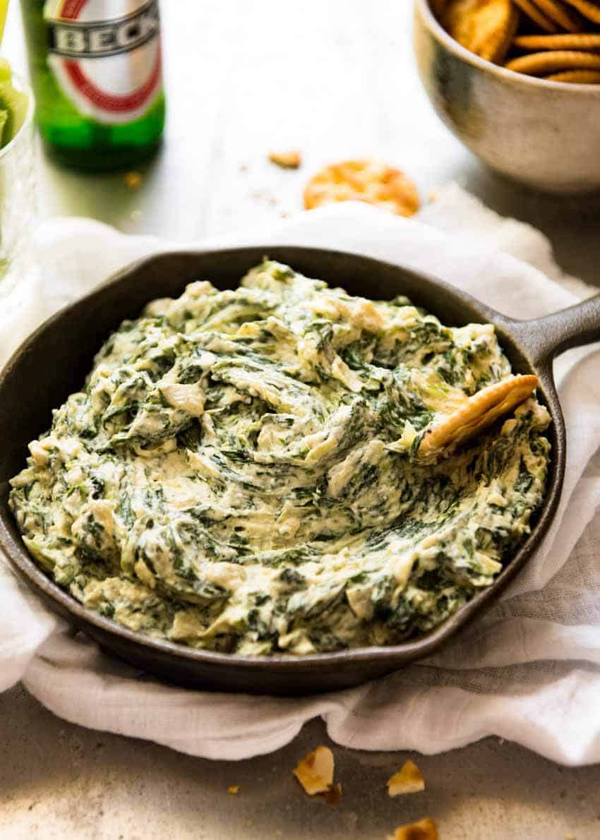 Spinach Artichoke Dip in a rustic black dish with a bowl of crackers for dipping