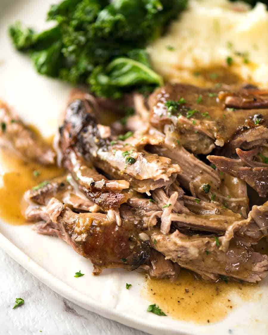 Tender Slow Roast Leg of Lamb with gravy on a plate with a side of potato and steamed greens