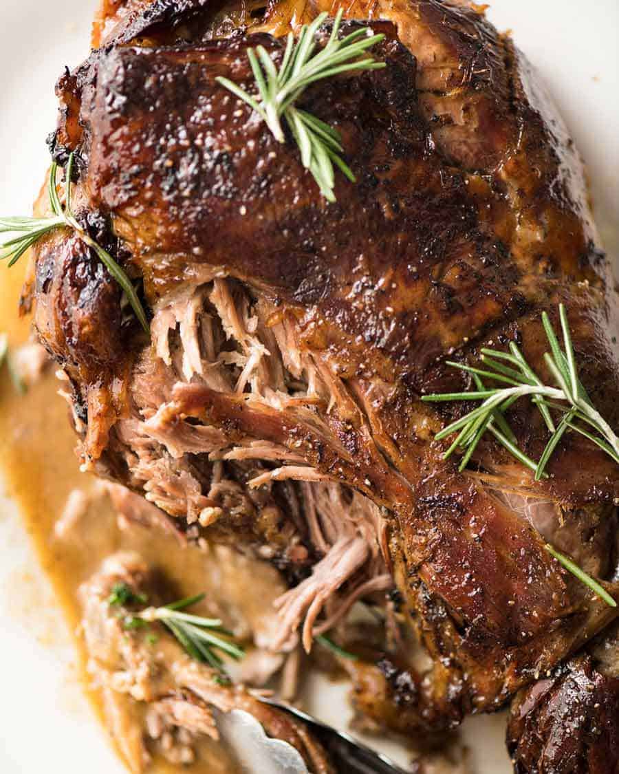Close up of Slow Roast Leg of Lamb on a white plate, garnished with rosemary sprigs