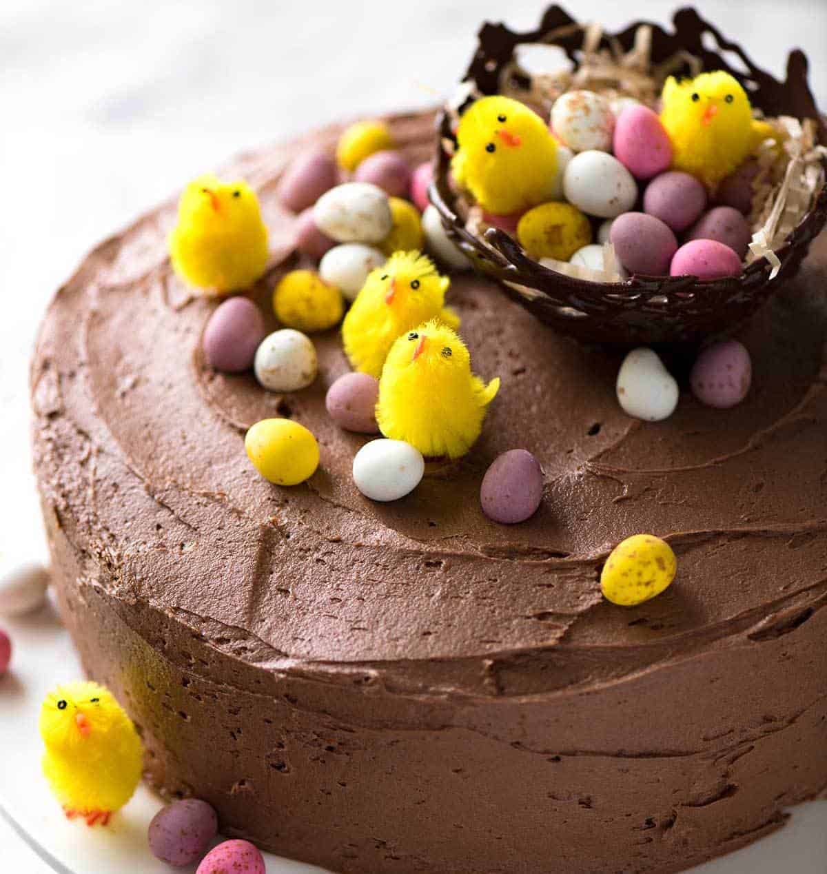 A Chocolate Cake with Buttercream Frosting decorated with small speckled Easter eggs and tiny fluffy yellow chicks.