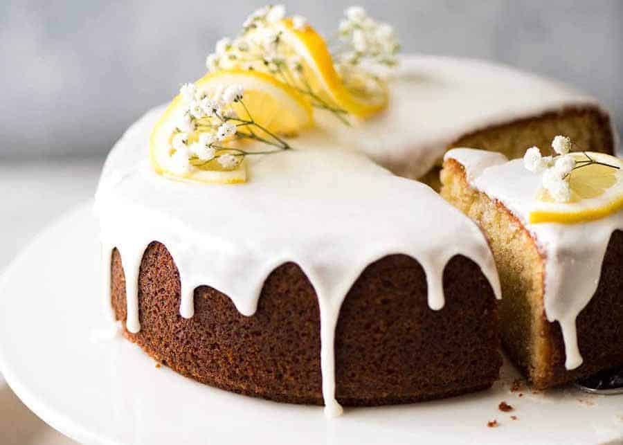 Lemon Cake with drippy lemon glaze on a white cake platter with a piece cut out