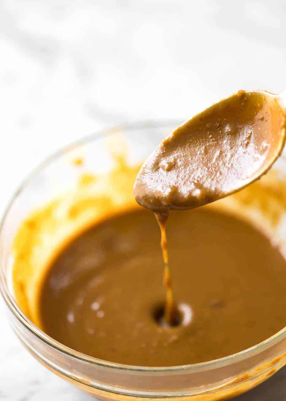 Spoon drizzling Satay Sauce for stir fries into mixing bowl