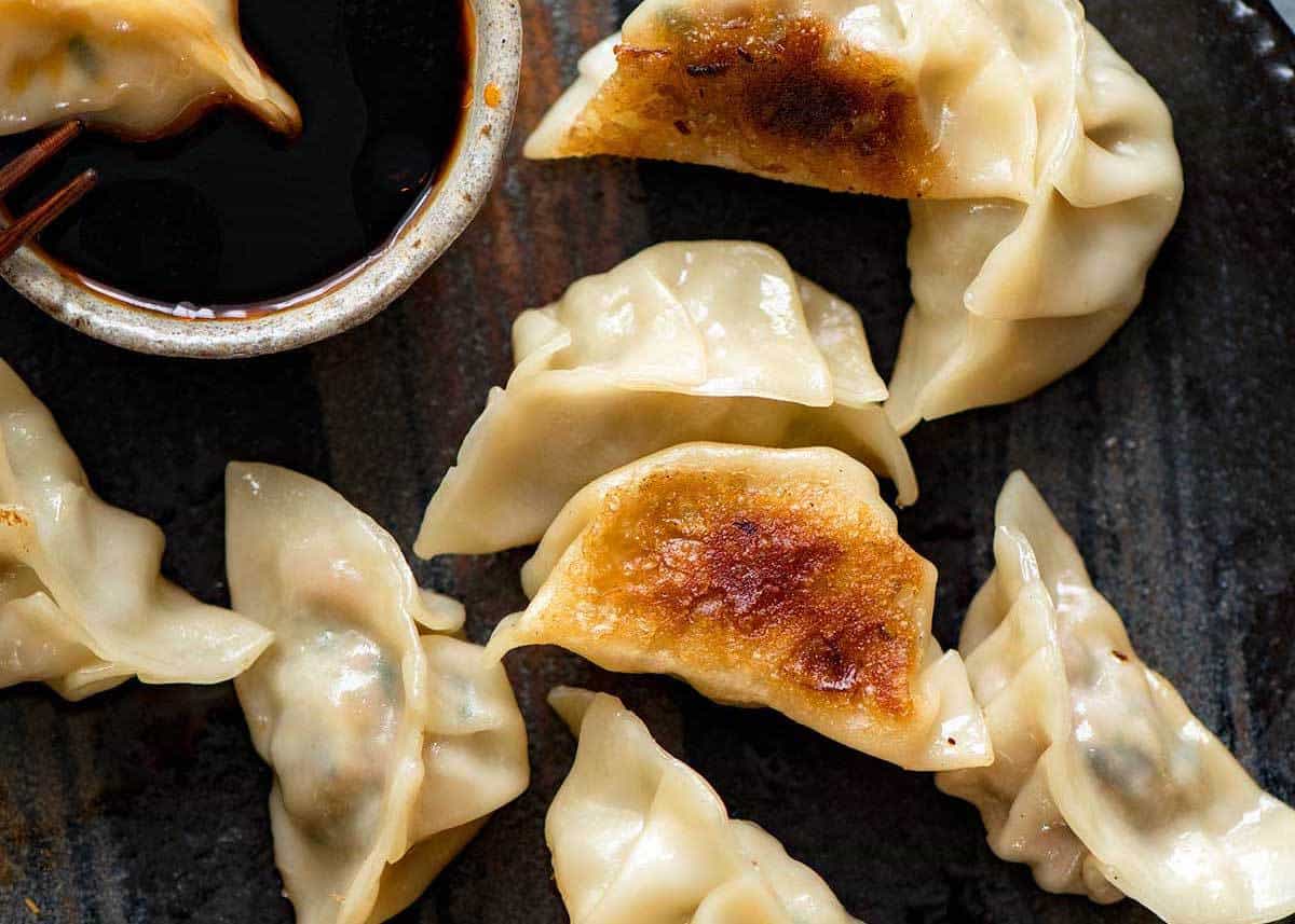 Overheat photo of Potstickers, also known as Pan Fried Chinese Dumplings, on a dark brown plate with dipping sauce.