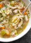 Close up of chicken and rice soup in a rustic beige bowl, ready to be eaten.