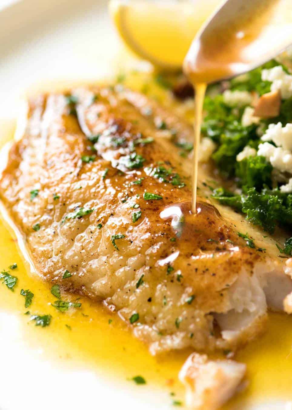 Lemon Butter Sauce being poured over crispy pan fried fish on a white plate.
