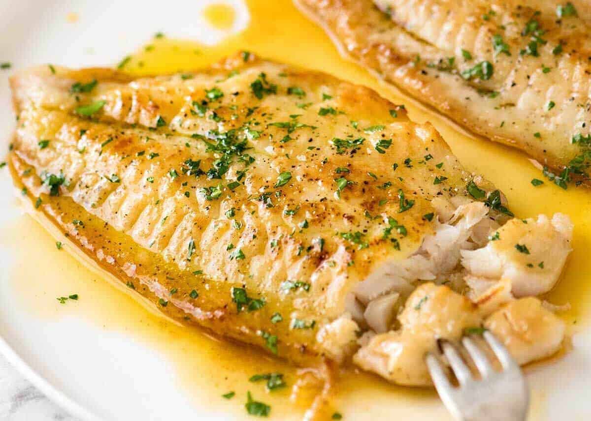 Close up photo of Crispy Pan Fried Fish with Lemon Butter Sauce and a sprinkle of parsley on a white plate.