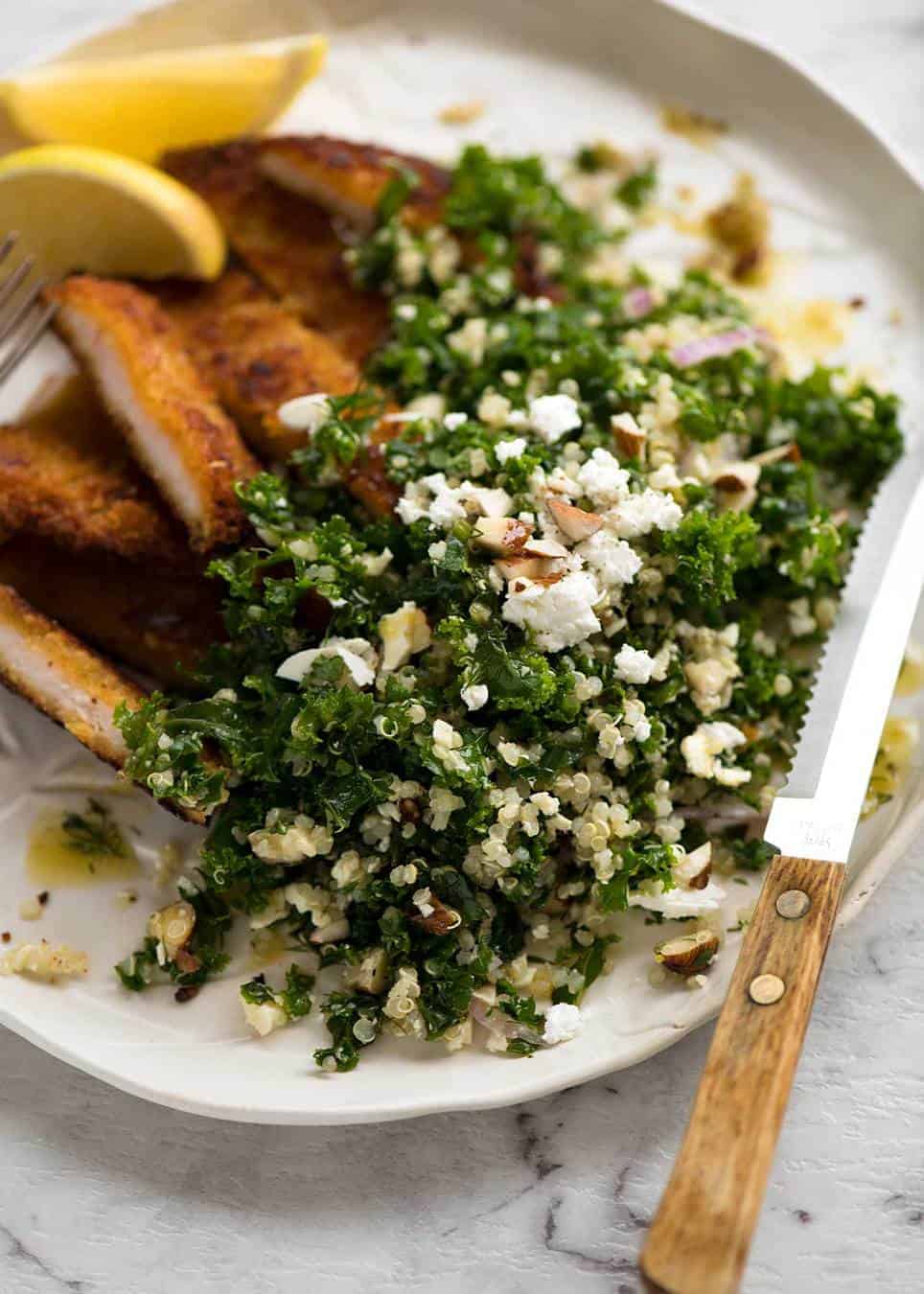 Kale and Quinoa Salad om a rustic white plate with cut up chicken schnitzel on the side, ready to be eaten.
