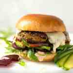 Un burger vegetarian cu brânză topită, avocado, sfeclă roșie, roșii și salată pe o chiflă moale și aurie.